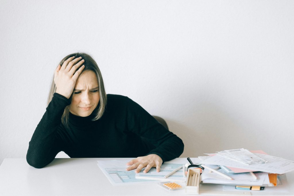 Woman in black sweater stressed with financial paperwork, overwhelmed at white table.